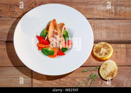 Fisch mit Gemüse auf einem weißen Teller auf dem Hintergrund einer hölzernen Tisch. Stockfoto