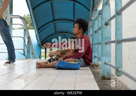 Ein verkrüppelter Mann sitzt mit einem Kind auf einem Gehweg in Cebu City, Philippinen um Geld betteln von Passanten Stockfoto