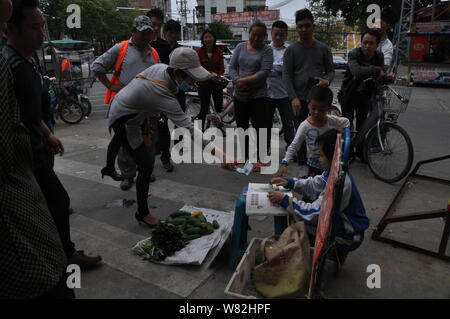 Ein Passant spendet 10 Yuan (1,45 $) zu neun Jahre alten chinesischen Mädchen Mao Mao, als sie Gemüse an einem strassenrand in Tangsha Stadt stall verkauft, Dongguan City, s Stockfoto