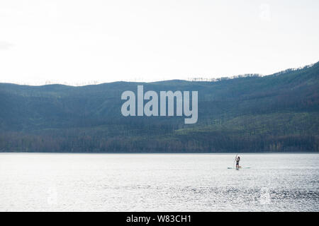 Junges Mädchen Stand up Paddle Boarding auf einem See McDonald im Glacier National Park Stockfoto