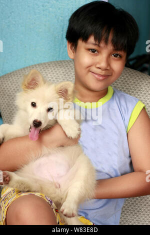 Portrait einer jungen Hübschen asiatischen Jungen mit einem niedlichen weißen Welpen. Stockfoto