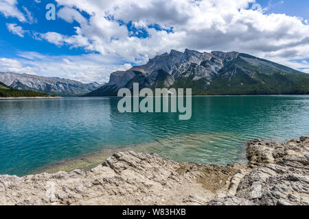 Die Feder am Lake Minnewanka - ein Frühling Blick auf bunte Lake Minnewanka, die von felsigen Küsten und rauen Berggipfeln umgeben, Banff National Park. Stockfoto