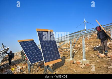 ------ Chinesische Arbeiter installieren Solaranlagen vor windenergieanlagen an einer Photovoltaik- Kraftwerk in Yiyang County, Luoyang City, Central Chinas Stockfoto