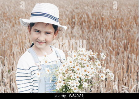 Glücklich süße kleine Mädchen mit einem Blumenstrauß aus Gänseblümchen auf einem Tau Feld Hintergrund Stockfoto