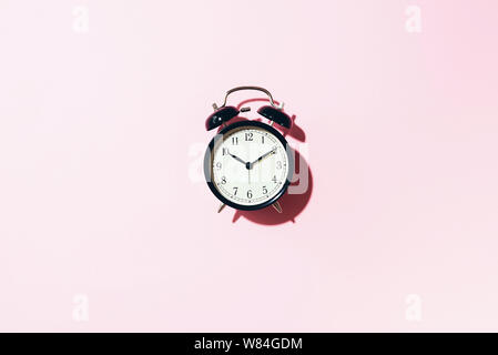 Schwarz Wecker mit harten Schatten auf rosa Hintergrund. Ansicht von oben. Stockfoto