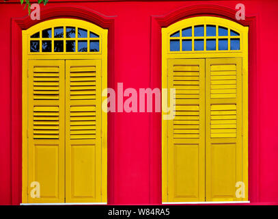 Nahaufnahme von Vintage Rundbogenfenster mit antiken gelben Fensterläden aus Holz rot Außenwand der traditionellen Singapur Shophouse im historischen Chinatown Stockfoto