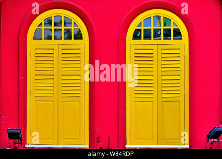 Nahaufnahme von Vintage Rundbogenfenster mit antiken gelben Fensterläden aus Holz rot Außenwand der traditionellen Singapur Shophouse im historischen Chinatown Stockfoto