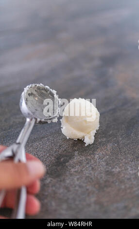 Ein Löffel setzen eine Kugel Vanilleeis auf einem Tisch aus Stein - lecker Eis - Bild vertikal Stockfoto