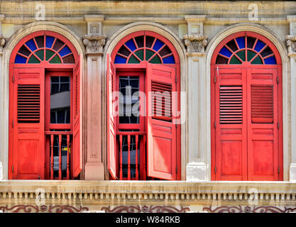 Nahaufnahme von Vintage Rundbogenfenster mit antiken roten Fensterläden aus Holz auf weiße Fassade des traditionellen Singapur Peranaka Shophouse in Little India Stockfoto