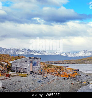 Anzeigen eines verlassenen Hauses und die patagonische Bergwelt von einer Insel von braun und orange Vegetation auf den Beagle Kanal, in der Nähe der Stadt Stockfoto