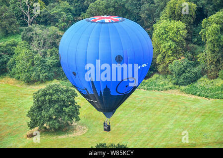Ein Ballon schwimmt über Ashton Hof Immobilien in der ersten Donnerstag Masse aufstieg Bristol International Balloon Fiesta, Bristol, wo hunderte von Ballons hoffen, über das Wochenende vor der vorhergesagten Stürme über England zu fliegen. Stockfoto