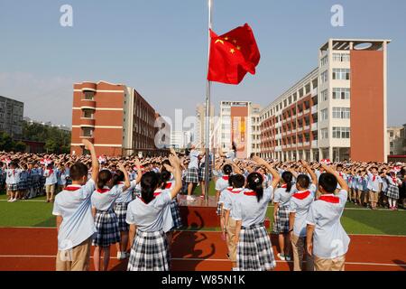 Junge chinesische Studenten grüßen während einer Flagge - Anhebung Zeremonie an einer Grundschule am ersten Tag des neuen Semesters in Lanzhou City, East China" Stockfoto