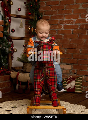 Kleines Baby auf Schaukelpferd, in Pullover und Jeans gekleidet. Weihnachten und neues Jahr Dekorationen Stockfoto