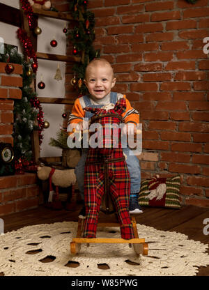 Kleines Baby auf Schaukelpferd, in Pullover und Jeans gekleidet. Weihnachten und neues Jahr Dekorationen Stockfoto