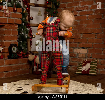 Kleines Baby auf Schaukelpferd, in Pullover und Jeans gekleidet. Weihnachten und neues Jahr Dekorationen Stockfoto