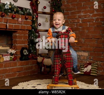 Kleines Baby auf Schaukelpferd, in Pullover und Jeans gekleidet. Weihnachten und neues Jahr Dekorationen Stockfoto