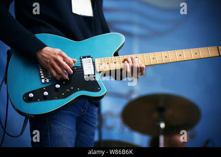 Ein Musiker in einem schwarzen T-Shirt und Blue Jeans spielt eine cooler Track auf einem blauen 6-String E-Gitarre, die bei einem Konzert. Stockfoto