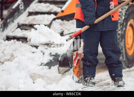 Schneeräumen in der Stadt. Arbeitnehmer hilft Schaufel Schneepflug. Stockfoto