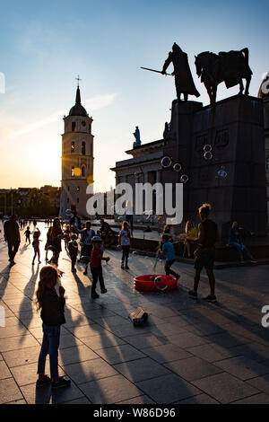 Abend am Platz der Kathedrale mit Glockenturm auf dem Hintergrund und den Sonnenuntergang mit Kindern spielen unter dem Gediminas Statue Stockfoto