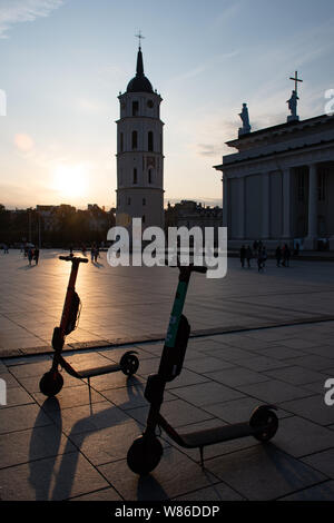 Vilnius, Litauen. Abend am Platz der Kathedrale mit Glockenturm auf dem Hintergrund und den Sonnenuntergang mit Elektroroller für Mieten, städtischer Verkehr Stockfoto