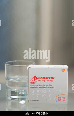 Carrara, Italien - August 08, 2019 - Box von Augmentin pills (Amoxicillin, Clavulanic acid) auf einem Glastisch, mit einem Glas Wasser und einer Pille bereit, Stockfoto