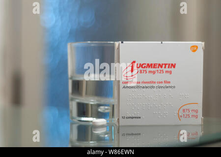 Carrara, Italien - August 08, 2019 - Box von Augmentin pills (Amoxicillin, Clavulanic acid) auf einem Glastisch, mit einem Glas Wasser und einer Pille bereit, Stockfoto