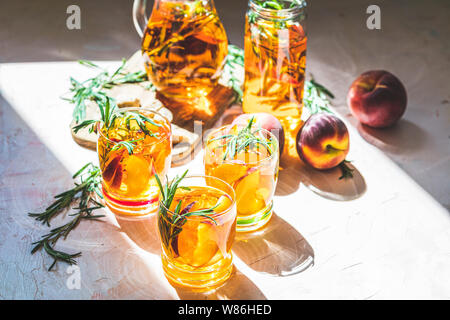 Gläser süßer Pfirsich Eistee, Sommer kalt Pfirsich fizz Cocktail mit Rosmarin. Sonnigen Licht. Geringe Tiefe des Feldes, Nahaufnahme, kopieren Sie Raum für Sie Stockfoto