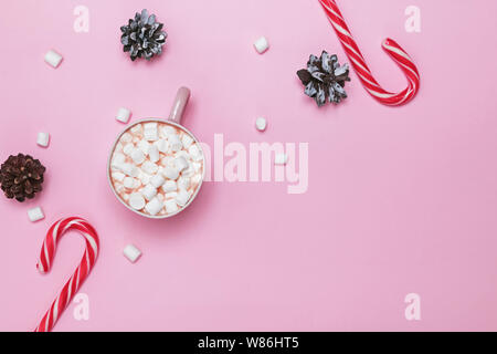 Weihnachten flach mit Kakao und Marshmallows, Zuckerstangen und Tannenzapfen auf rosa Hintergrund Stockfoto