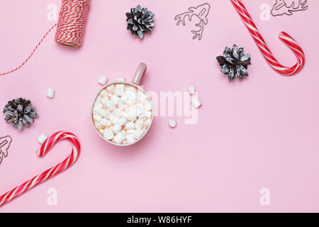 Weihnachten flach mit Kakao und Marshmallows, Zuckerstangen und Tannenzapfen auf rosa Hintergrund Stockfoto