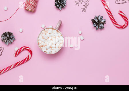 Weihnachten flach mit Kakao und Marshmallows, Zuckerstangen und Tannenzapfen auf rosa Hintergrund Stockfoto