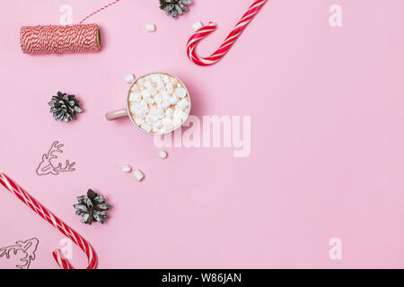 Weihnachten flach mit Kakao und Marshmallows, Zuckerstangen und Tannenzapfen auf rosa Hintergrund Stockfoto