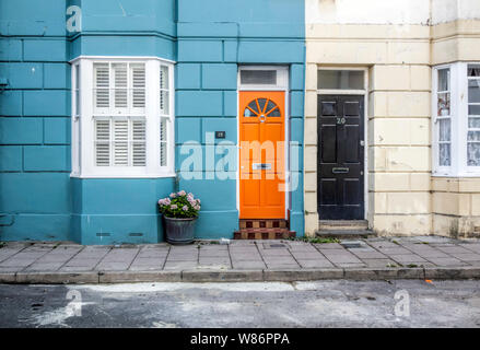 Frisch orange leuchtenden Tür mit blauen Mauer gemalt Neben schwarzen Tür auf der weißen Wand Conservation Area, über Street, Brighton East SussexUK Stockfoto