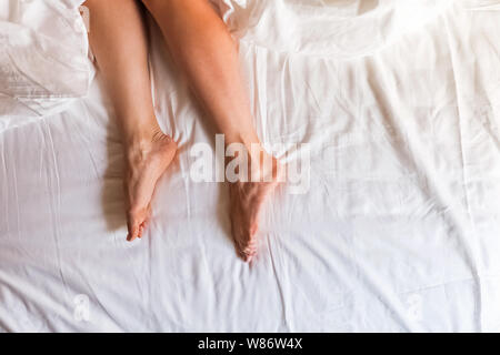 Woman's Beine auf dem Bett mit weißer Bettwäsche, Ansicht von oben Stockfoto