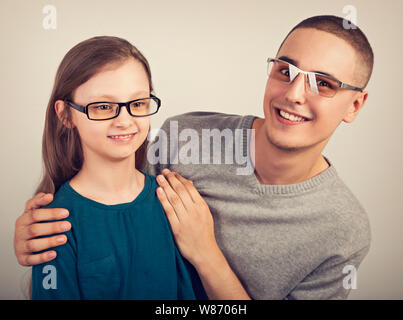 Glückliche junge positive Vater sein lächelndes nachdenklich Schulmädchen Kid Mode Brille auf der leere Raum Hintergrund umarmte. Closeup vintage Portrait Stockfoto