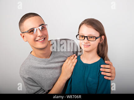 Glückliche junge positive Vater sein lächelndes nachdenklich Schulmädchen Kid Mode Brille auf der leere Raum Hintergrund umarmte. Closeup Portrait Stockfoto