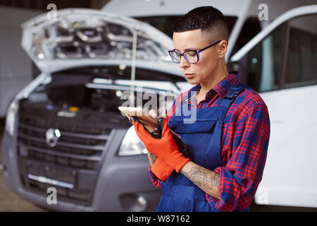 Weibliche Automechaniker überprüft, welche auf ihrem Tablet Bildschirm geschrieben ist Stockfoto