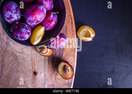 Lecker saftig blaue Pflaumen in einer Schale auf dem Tisch, strukturierte Holztisch, natürliche Materialien und natürliche umweltfreundliche Produkte, gesundes Essen. Stockfoto