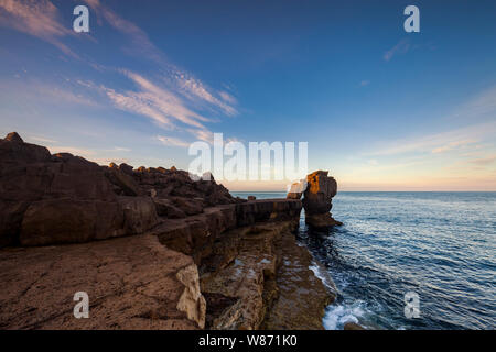 Die Sonne beleuchtet die Kanzel rock am frühen Morgen an der Portland, Dorset, England. Es ist ein ruhiges Meer mit blauem Himmel und Wolken. Stockfoto