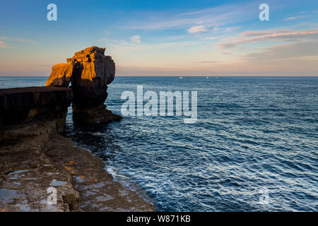 Die Sonne beleuchtet die Kanzel rock am frühen Morgen an der Portland, Dorset, England. Es ist ein ruhiges Meer mit blauem Himmel und Wolken. Stockfoto