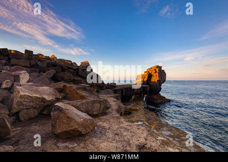 Die Sonne beleuchtet die Kanzel rock am frühen Morgen an der Portland, Dorset, England. Es ist ein ruhiges Meer mit blauem Himmel und Wolken. Stockfoto