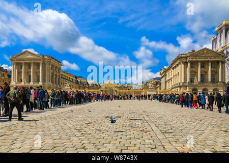 Tolle Aussicht auf eine große U-förmige Schlange der Besucher vor dem Schloss von Versailles im Golden Royal Tor im gepflasterten Hof der Ehre... Stockfoto