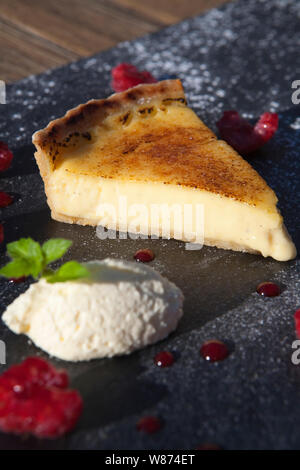 Hausgemachte lemon Tart mit Schlagsahne und Himbeeren auf schwarzem Schiefer in einem Fine Dining Restaurant serviert Stockfoto