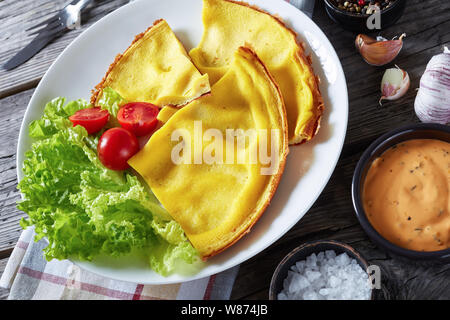 Close-up geschnittenes Omelett auf einem weißen Teller mit Salat und frische Tomaten auf einem alten rustikalen Holztisch, horizontale Ansicht von oben Stockfoto