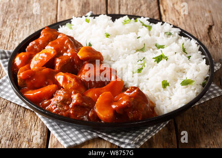 Würziges Rindfleisch mit Äpfeln in Tomatensauce mit Reis Beilage schließen gekocht - bis auf einen Teller auf dem Tisch. Horizontale Stockfoto