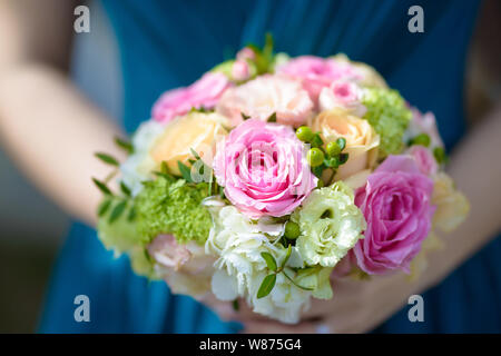 Brautjunfer gekleidet in einem blauen Kleid, die eine runde bunte Wedding Bouquet mit frischen Rosen, wilde Blumen und Grün Stockfoto