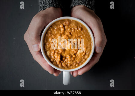 Hohe Betrachtungswinkel und einer jungen kaukasischen Mann mit einer Schüssel mit Linsensuppe in der Hand auf einem grauen Tabelle Stockfoto
