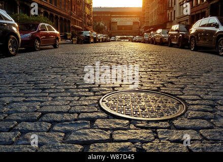 Sonnenlicht auf einer Straße mit Kopfsteinpflaster und Kanaldeckel in Manhattan New York City NYC Stockfoto