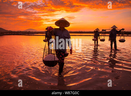 Frau Arbeiter die Körbe der frisch geerntete Salz auf ihren Schultern in Hon Khoi Salz Feld bei Sonnenaufgang, Nha Trang Provinz, Vietnam Stockfoto