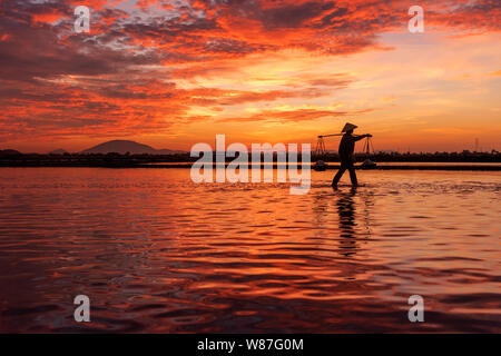 Frau Arbeiter die Körbe der frisch geerntete Salz auf ihren Schultern in Hon Khoi Salz Feld bei Sonnenaufgang, Nha Trang Provinz, Vietnam Stockfoto