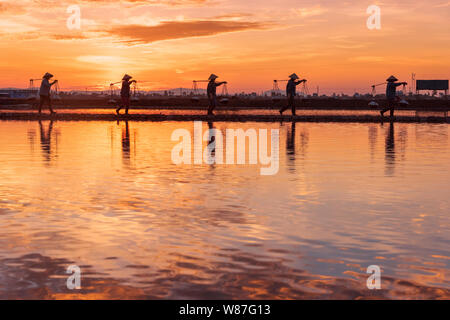 Frau Arbeiter die Körbe der frisch geerntete Salz auf ihren Schultern in Hon Khoi Salz Feld bei Sonnenaufgang, Nha Trang Provinz, Vietnam Stockfoto